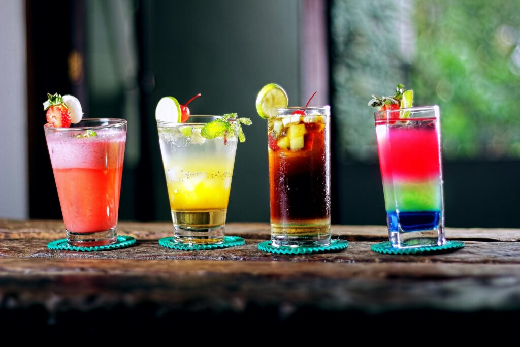 Colorful assortment of cocktails on a rustic wooden table, perfect for a refreshing summer evening.